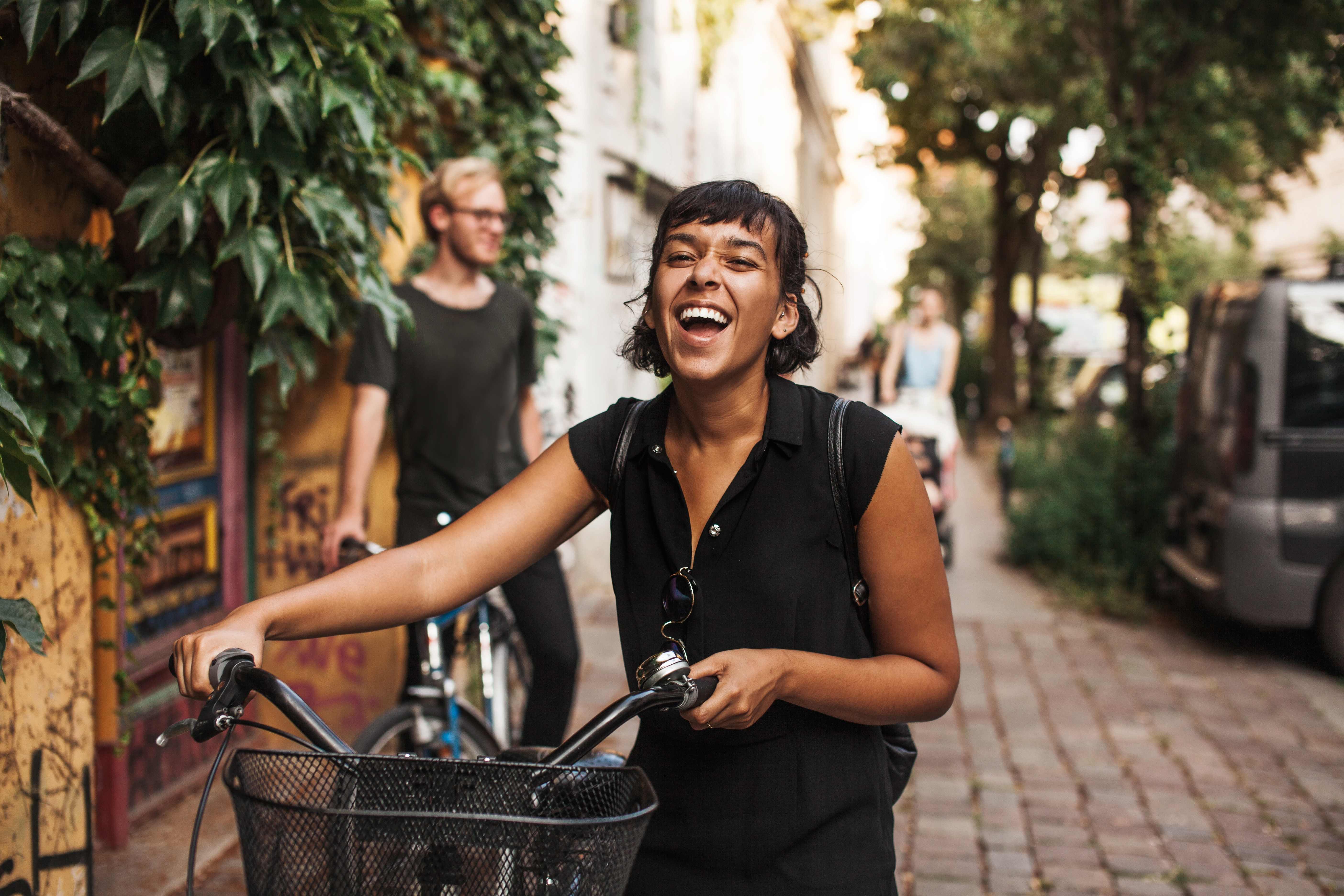 EYA_TR Laughing young woman walking her bike on brick sidewalk smaller