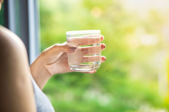 Woman holding glass of water near large glass window with nature view outside